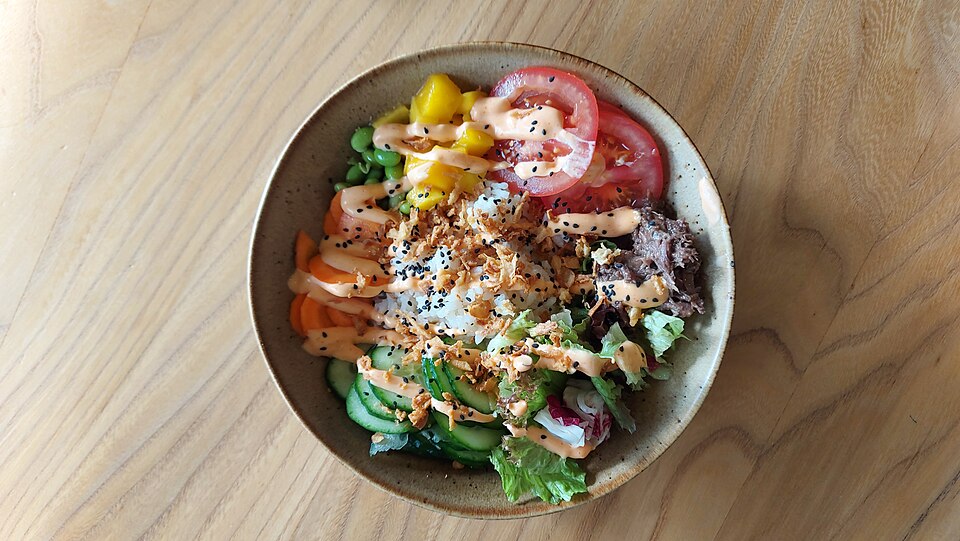 A colorful poké bowl with cubes of fresh raw fish, rice, and vegetables.